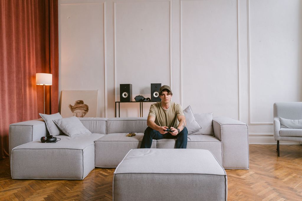 Man playing a console video game on a gray sectional sofa in a modern living room