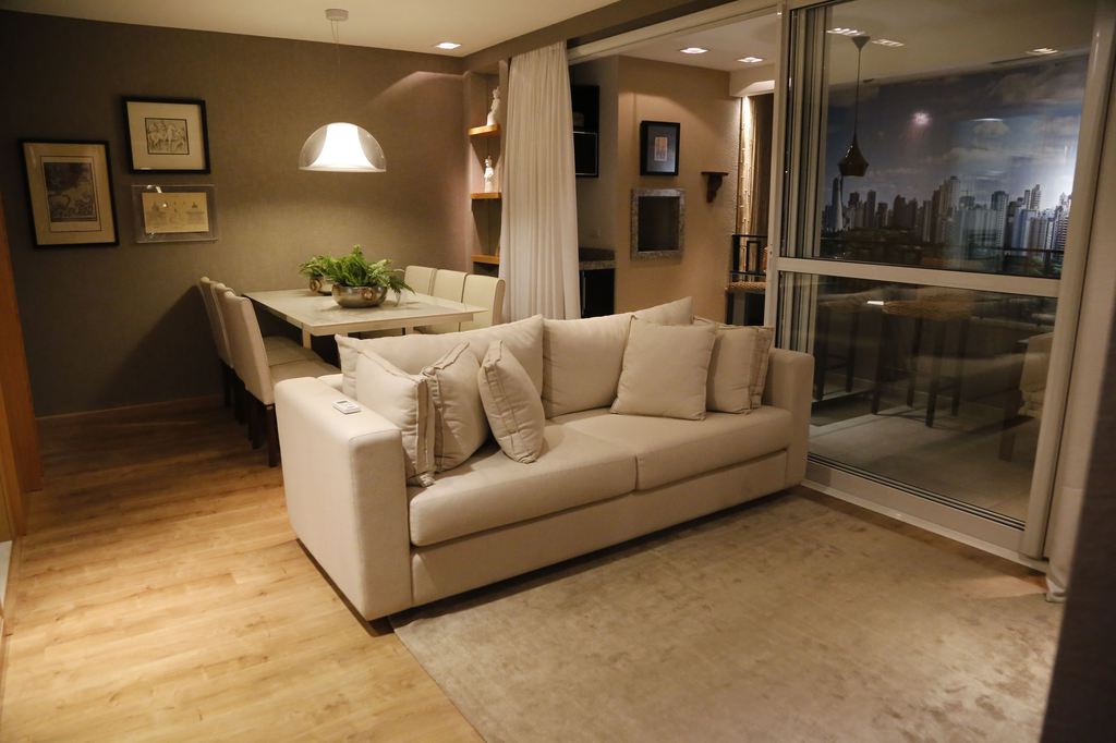 Light beige sofa in a modern open-plan living room with warm wood flooring, a dining area, and a city view.