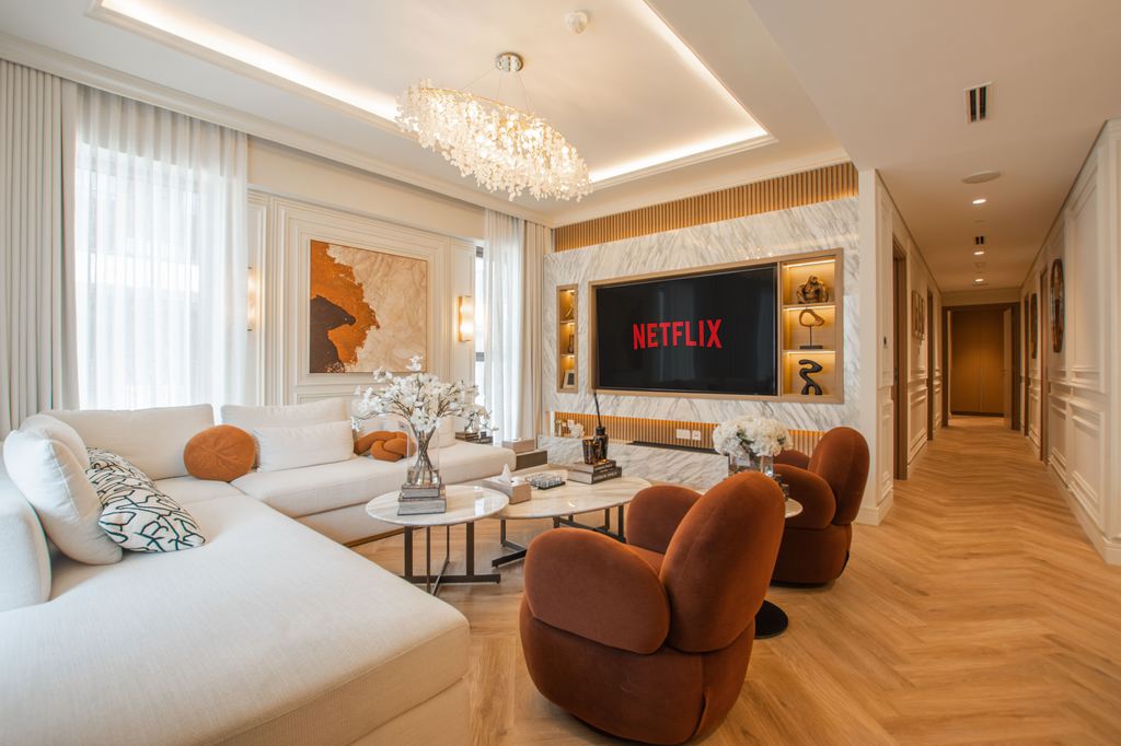 Modern living room home theater with a wall-mounted TV, curved sofas and chairs, marble media wall, and warm ambient lighting.