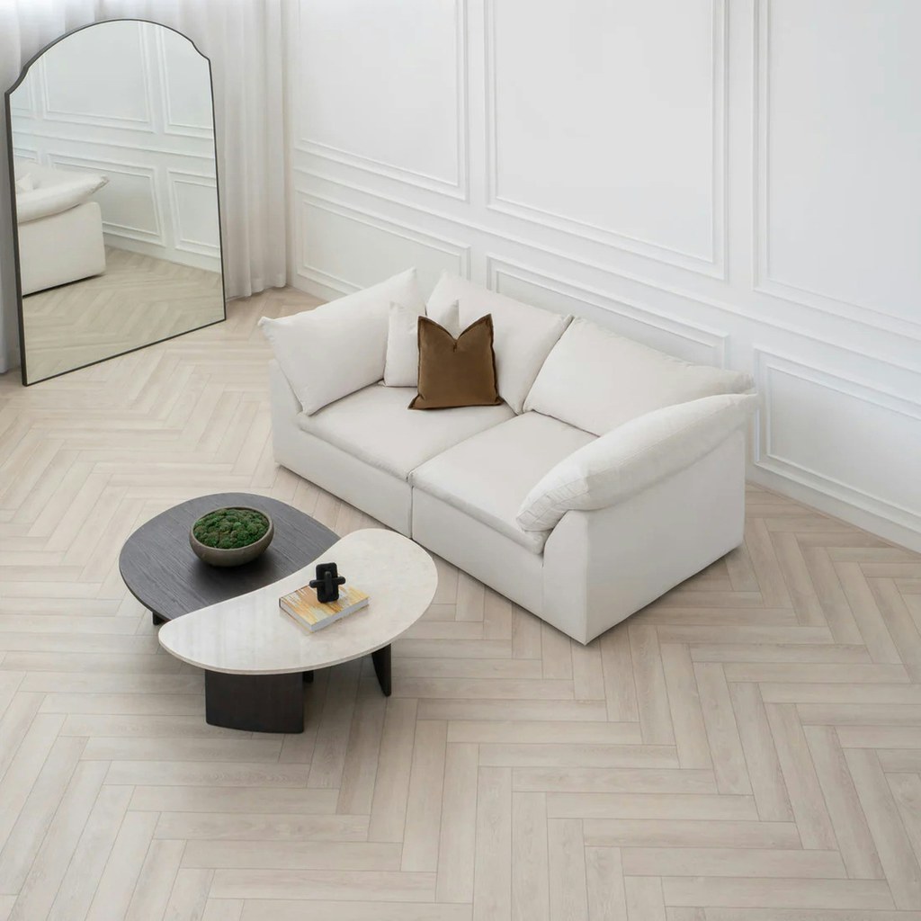 White loveseat in a minimalist living room with paneled walls, herringbone flooring, and nesting coffee tables.