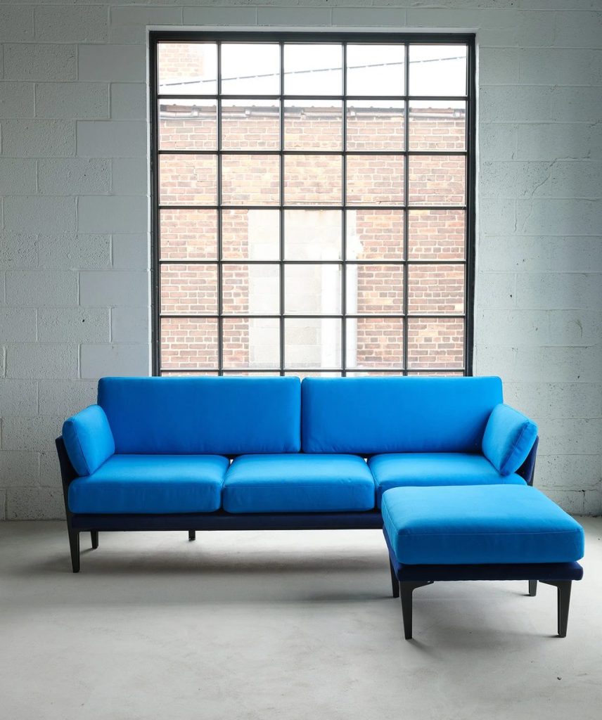 Blue three-seat sofa with a matching ottoman in a bright industrial-style apartment living room.