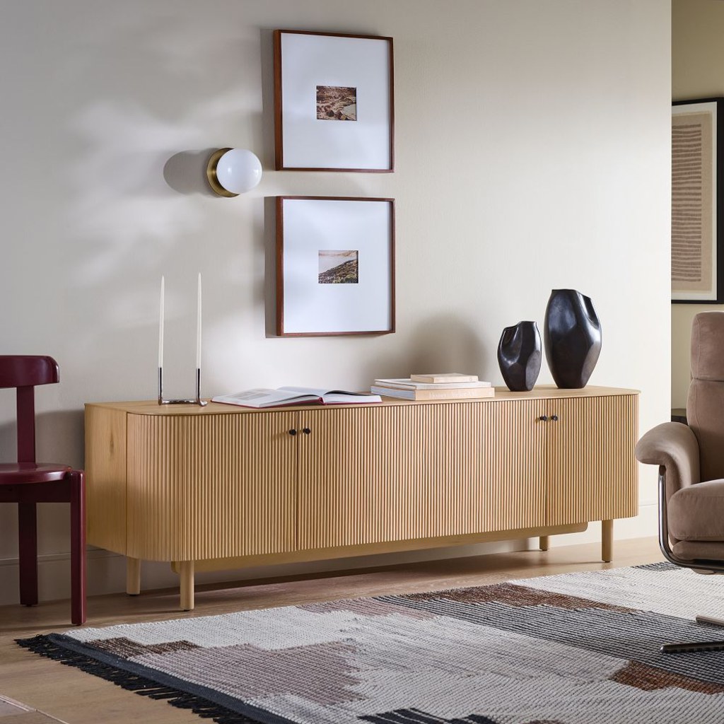 Light wood fluted media console with closed storage, books, decorative vases, and framed wall art.
