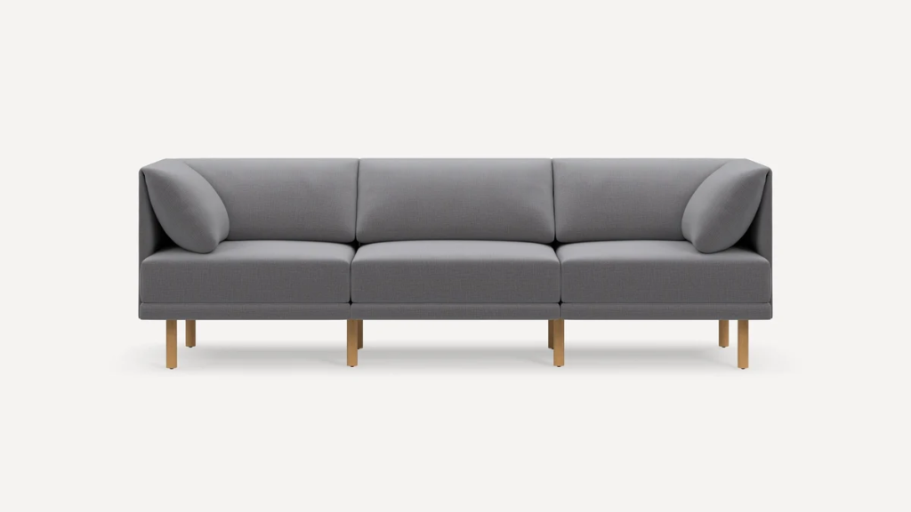 Gray three-seat modular sofa with slim wooden legs and two bolster pillows.