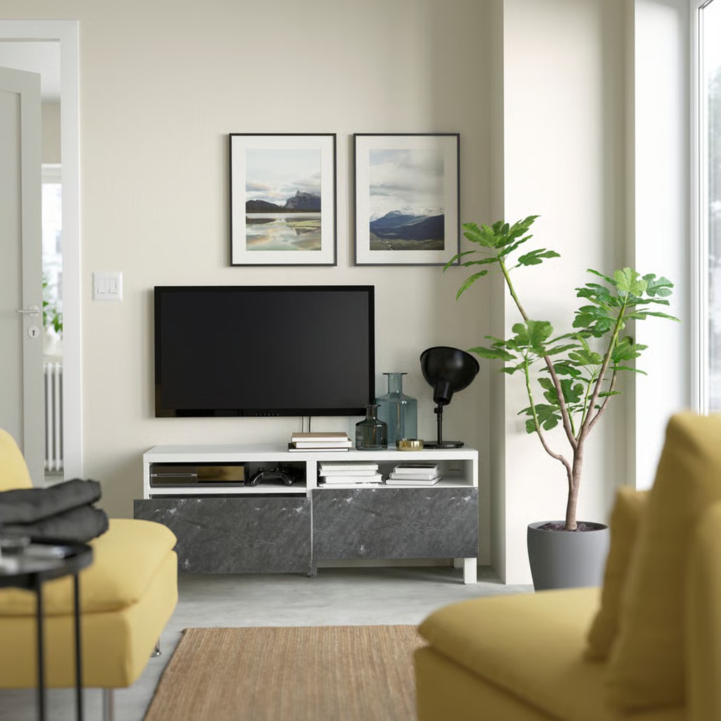 White and gray media console with open shelves beneath a wall-mounted TV in a modern living room with plants and yellow seating.