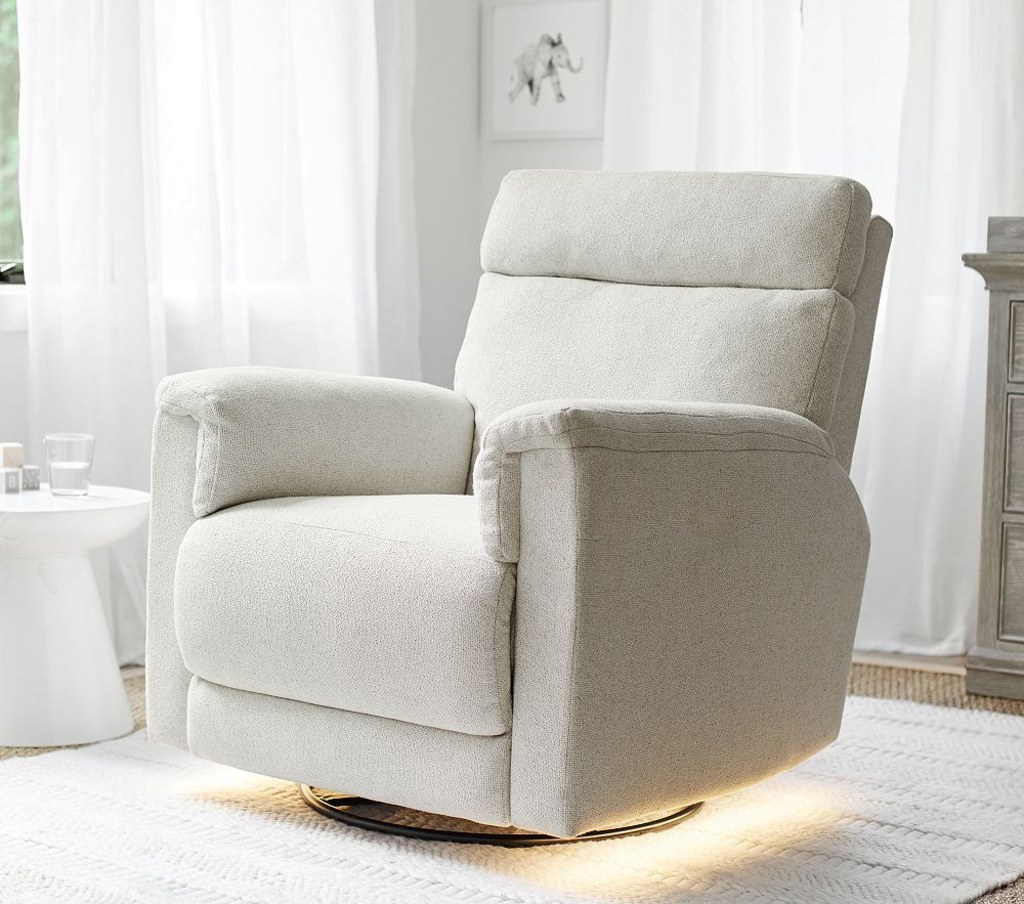 Cream upholstered swivel nursery recliner with padded arms and soft under-chair lighting in a bright neutral room.