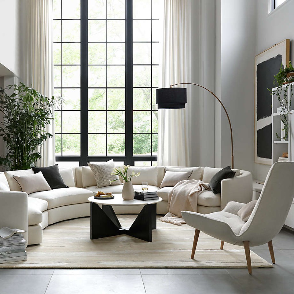 White curved sectional sofa in a bright modern living room with large windows, coffee table, and lounge chair.