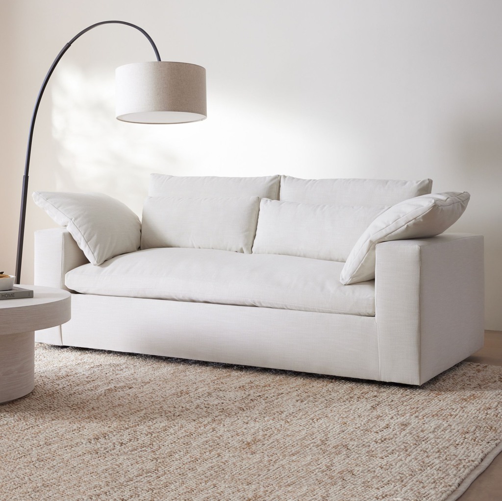 White sleeper sofa with oversized loose cushions, square arms, and a soft upholstered seat in a bright neutral living room.