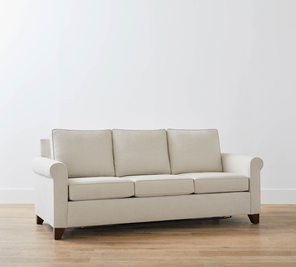 Beige roll-arm sleeper sofa with three seat cushions and matching back cushions on a light wood floor.