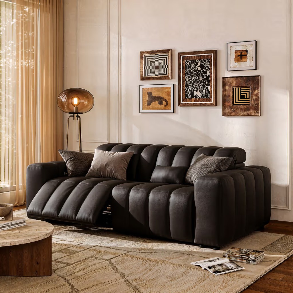 Black leather reclining sofa with tufted cushions in a warm modern living room with framed wall art and wood accents.