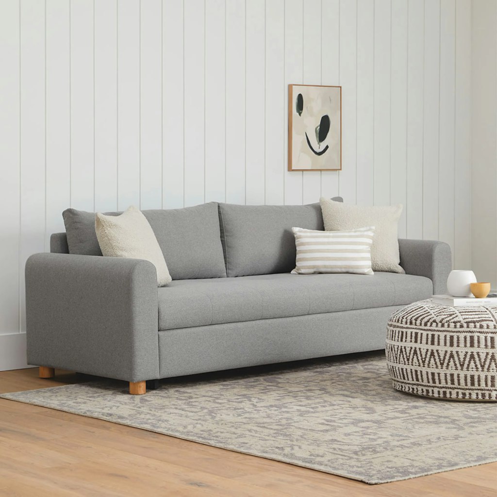 Gray sleeper sofa with plush back cushions and neutral accent pillows in a bright modern living room.