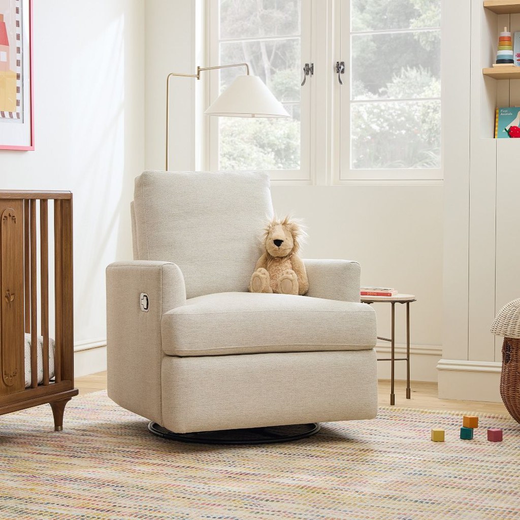 Beige swivel nursery recliner with a teddy bear beside a wooden crib in a bright baby room.