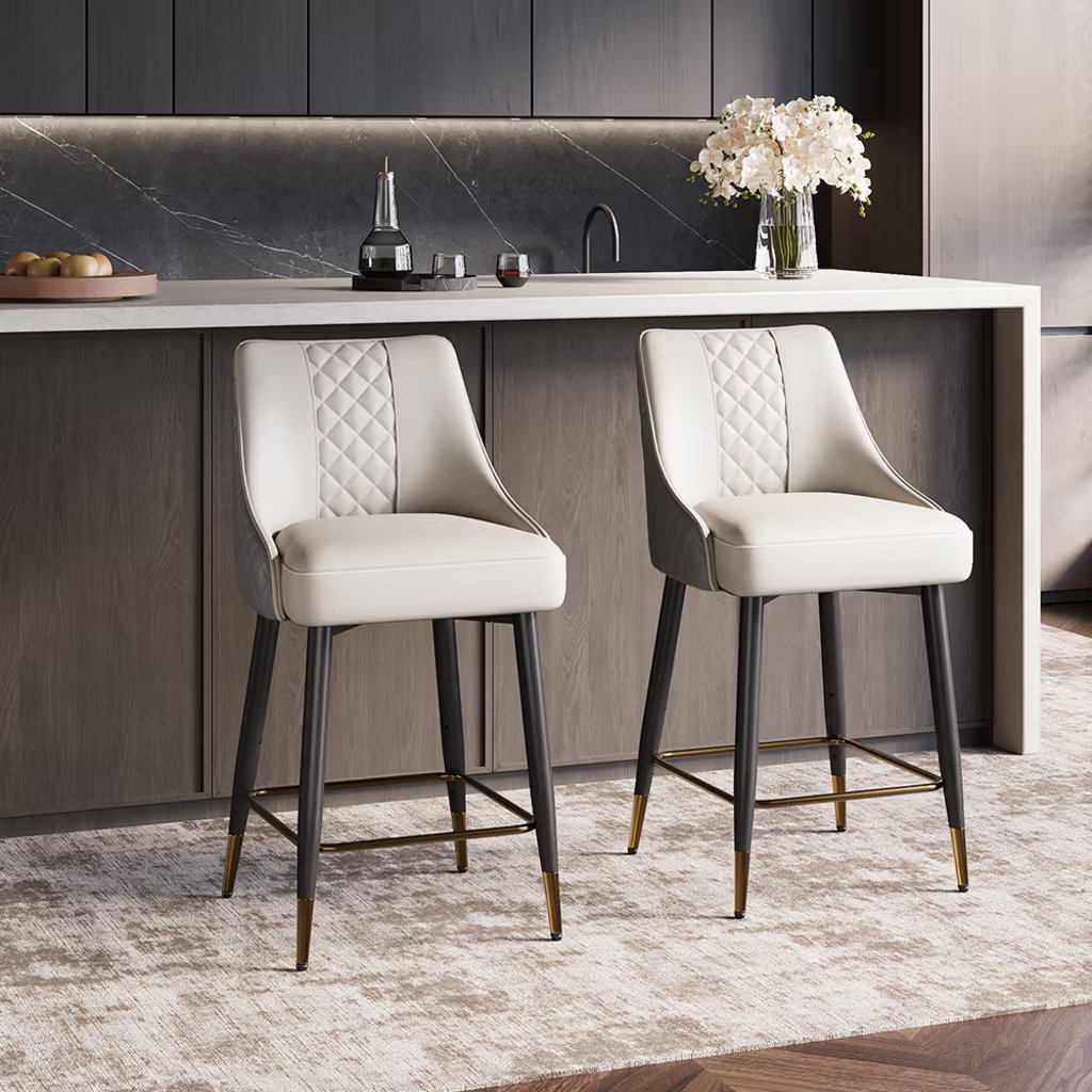 Two cream upholstered counter stools with black legs and gold footrests at a modern kitchen island.