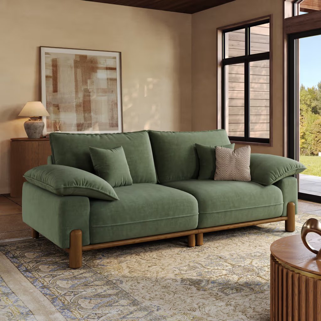 Green upholstered sofa with plush back and arm cushions in a warm modern living room.