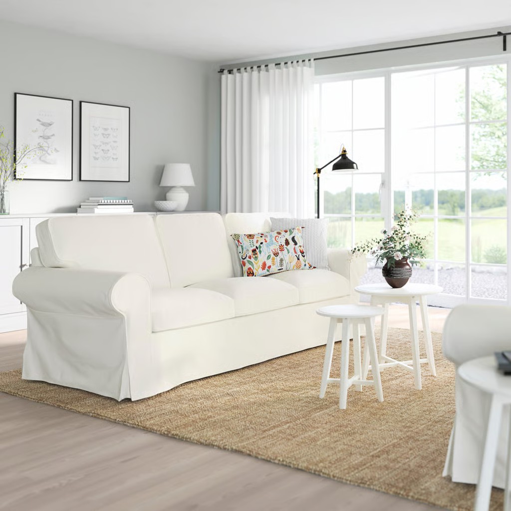 White slipcovered sofa with loose cushions in a bright living room with large windows and neutral decor.