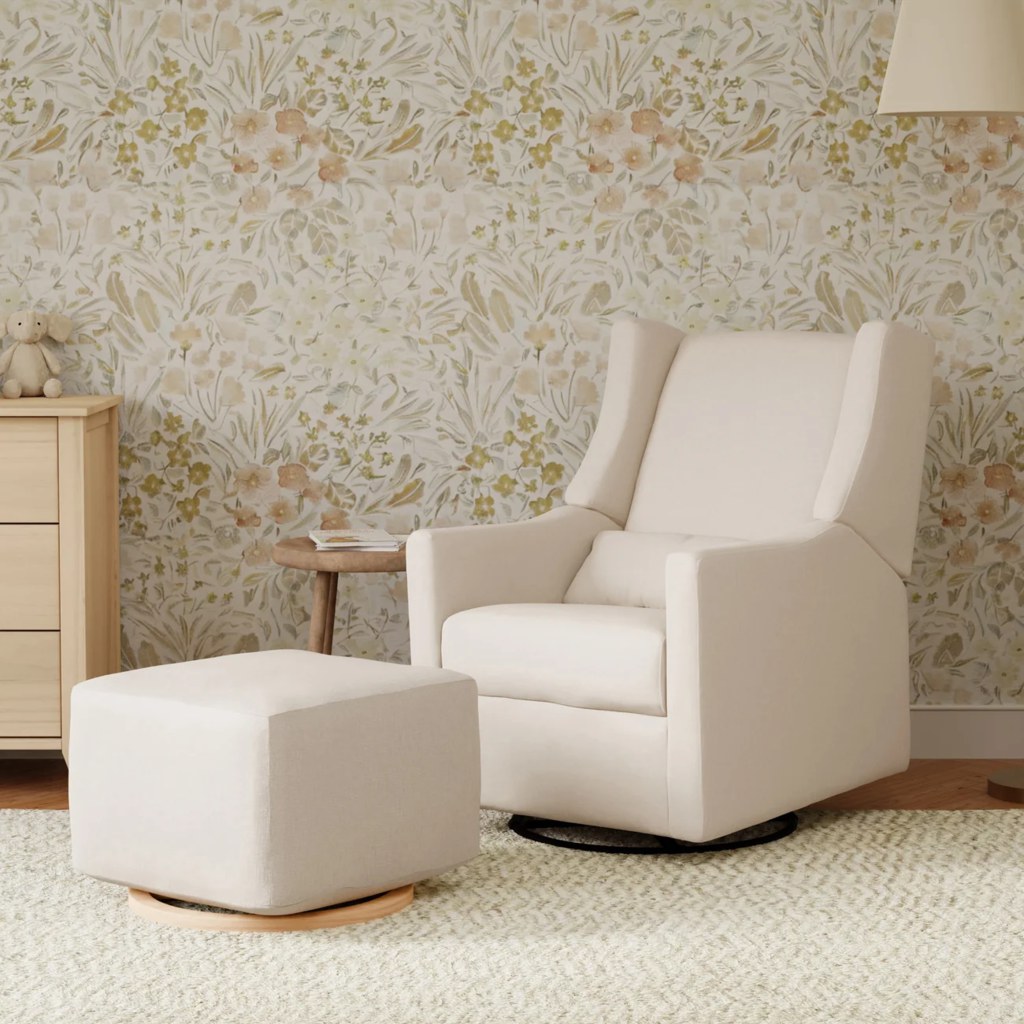 Cream swivel nursery recliner with matching ottoman in a softly decorated baby room with floral wallpaper.