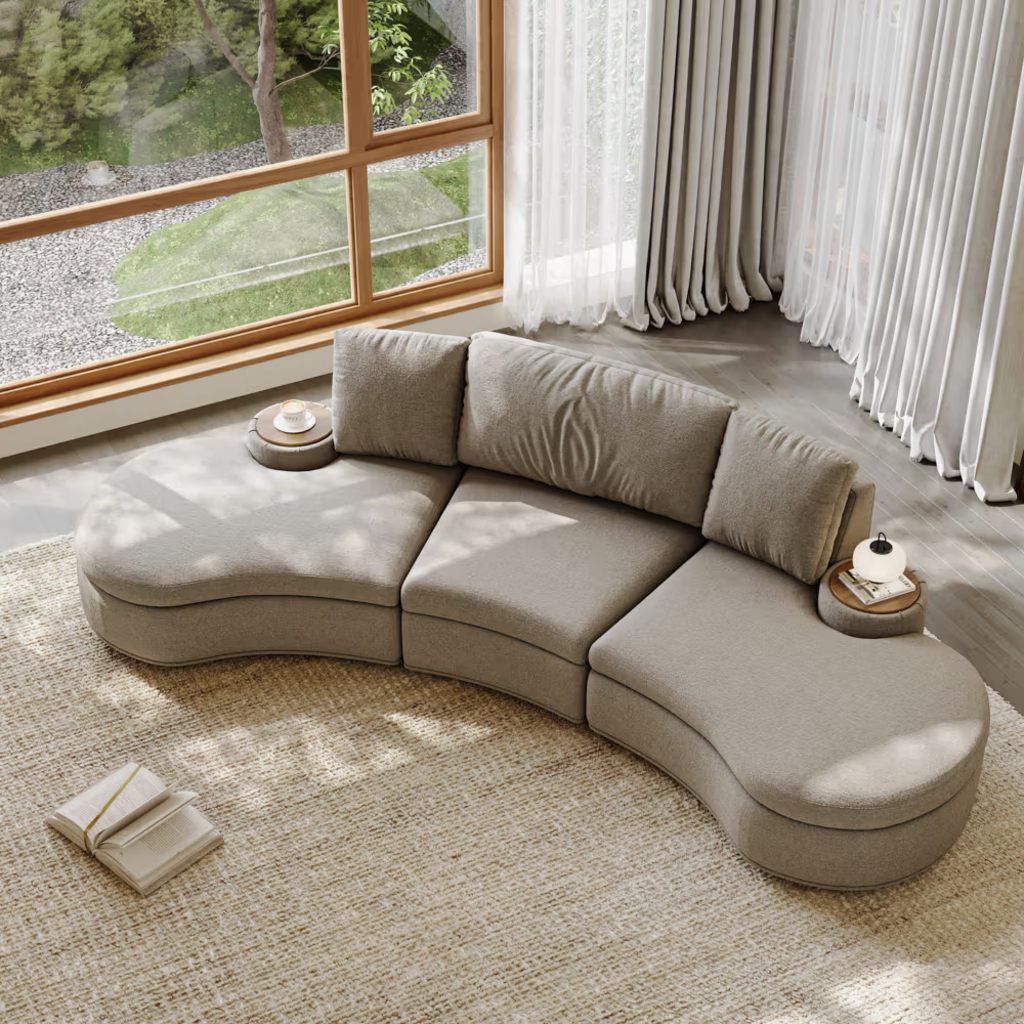 Beige curved sectional sofa with deep seats and side tables in a bright modern living room.