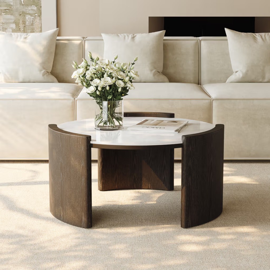 Round coffee table with a white stone top and curved dark wood base in a bright modern living room.