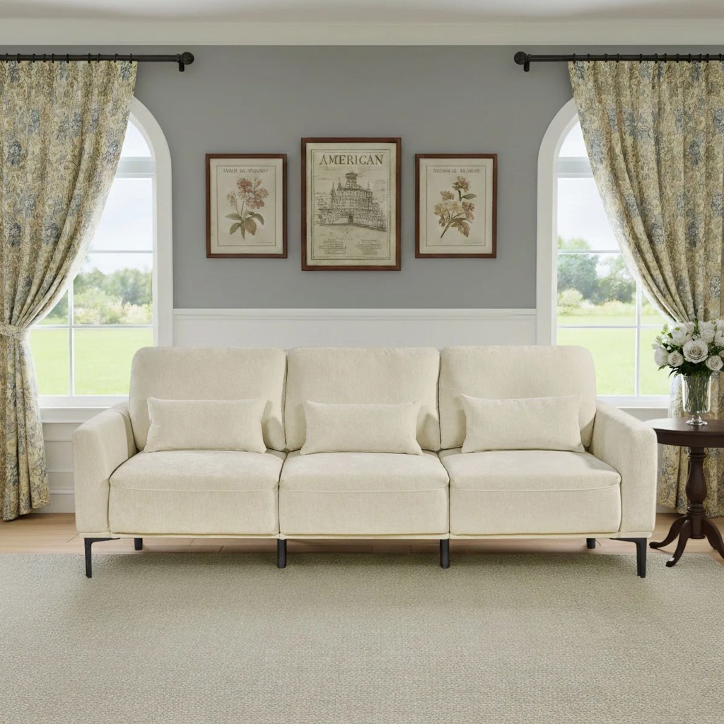 Cream three-seat adjustable-back sofa with lumbar pillows and slim black legs in a bright traditional living room.