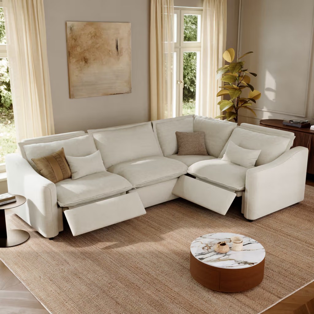 White modular sectional sofa with reclining footrests in a bright modern living room with large windows, neutral decor, and a round marble coffee table.