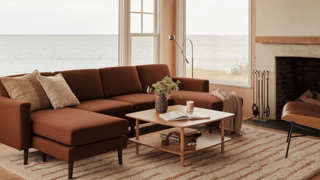 Brown modular sectional sofa with raised legs in a bright coastal living room with a fireplace and ocean view.