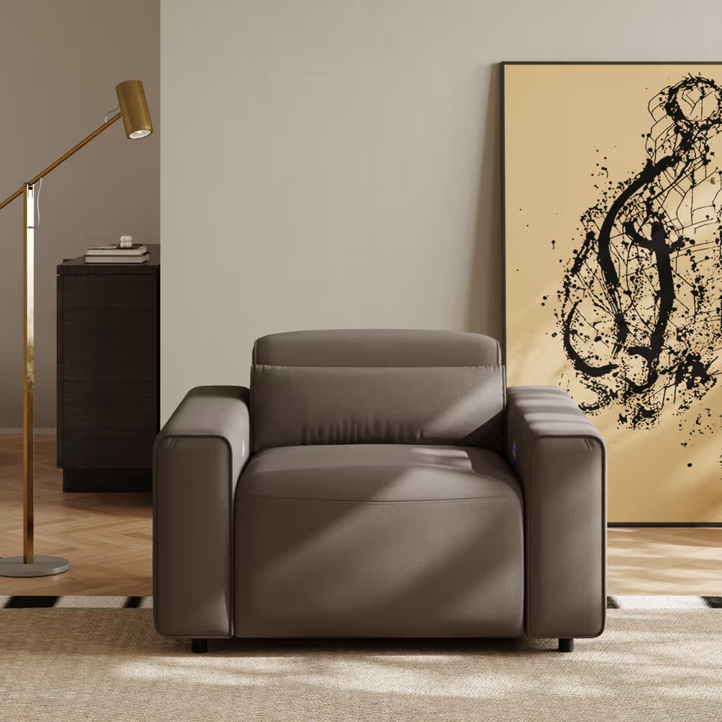 Brown leather power recliner chair with padded arms in a modern living room with a floor lamp and abstract wall art.