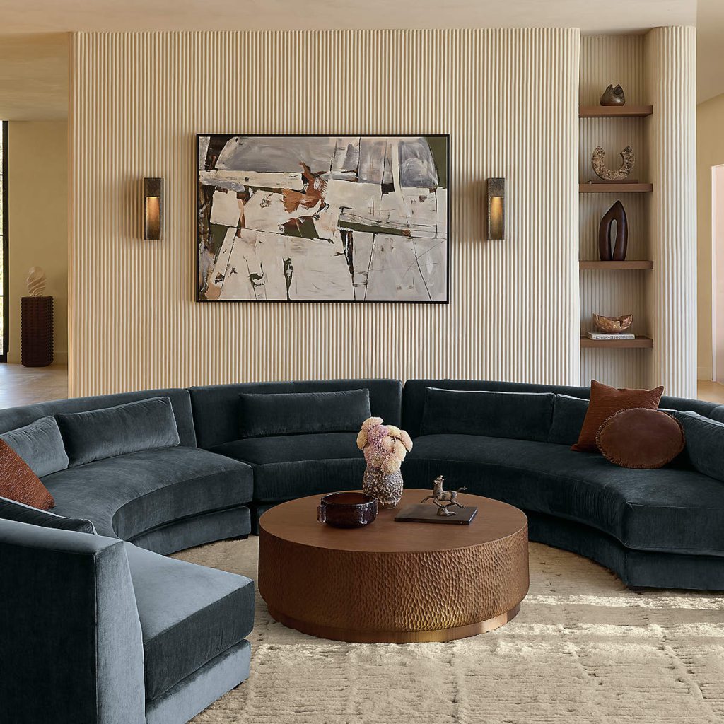 Dark curved sectional sofa in a modern living room with a wall-mounted TV, wood paneling, and round coffee table.