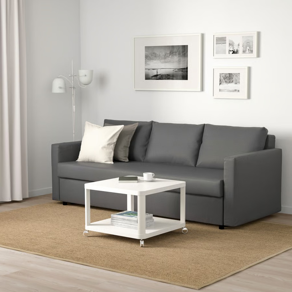 Gray sleeper sofa with loose back cushions and square arms in a modern living room with a wheeled white coffee table.