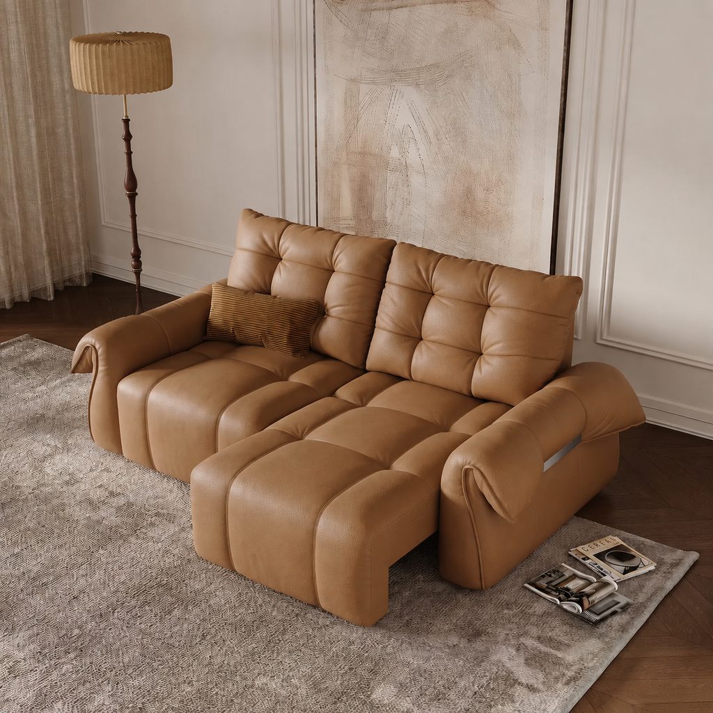Tan leather power sofa bed partially extended in a warm modern living room with tufted cushioning and a floor lamp.