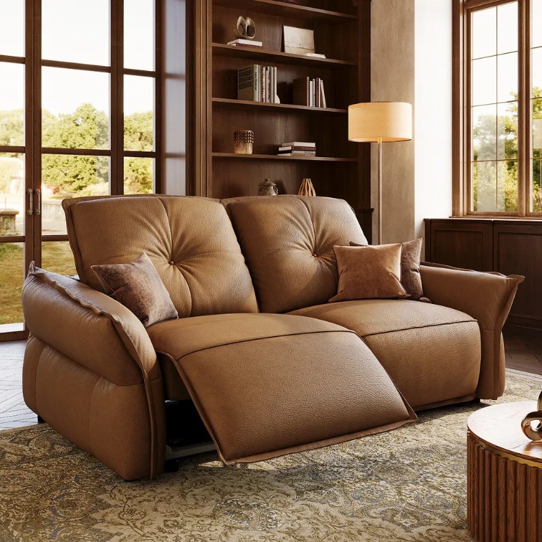 Brown dual-power reclining loveseat in a warm reading room with bookshelves, floor lamp, and large windows.