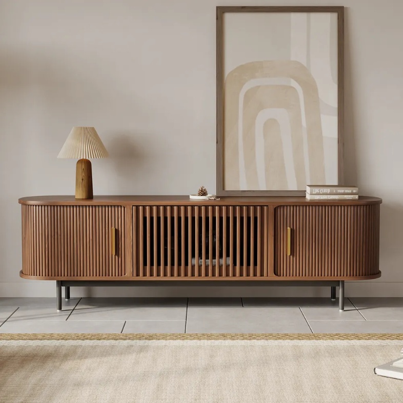 Walnut tambour-door media console with slatted center storage, a table lamp, framed artwork, and books.
