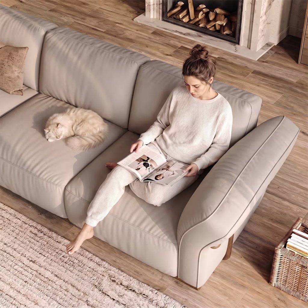 Cozy light-toned living room with a woman reading on a beige sofa beside a sleeping cat and fireplace.