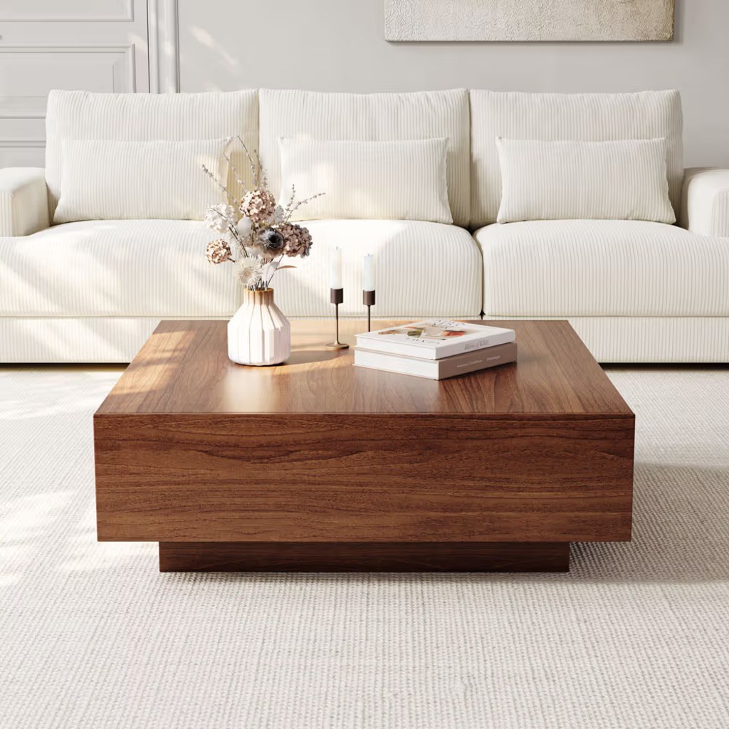Modern walnut coffee table placed in front of a white sofa in a minimalist living room with books and decorative accents.