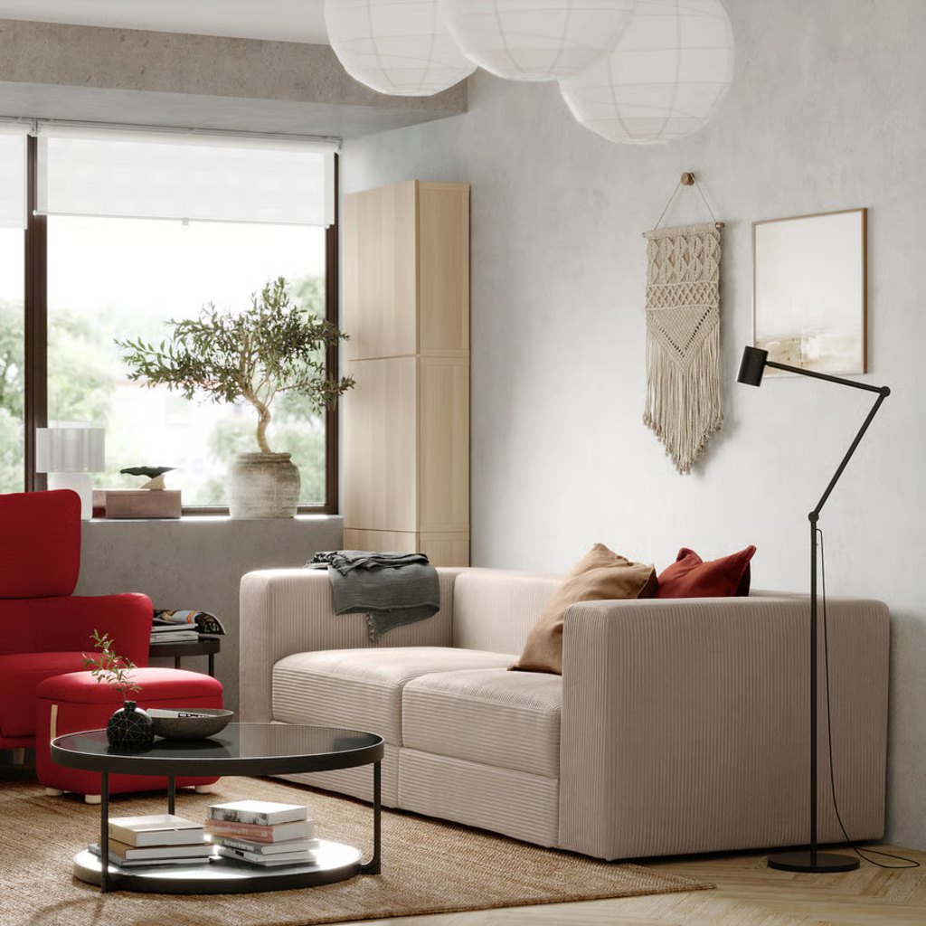 Beige two-seat sofa in a compact living room with a red armchair and round coffee table.