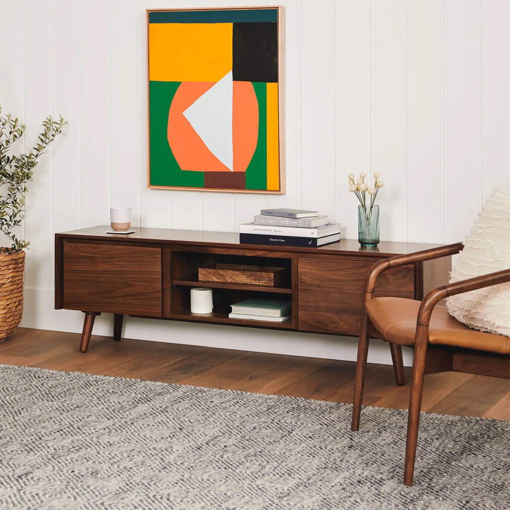 Mid-century walnut media console with open shelving, closed cabinets, books, decor, and abstract wall art.