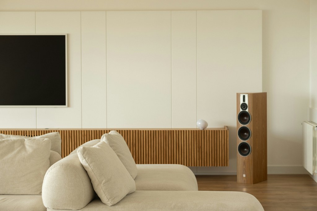 Beige sectional sofa in a modern living room with a wall-mounted TV, wood media console, and floor speaker.