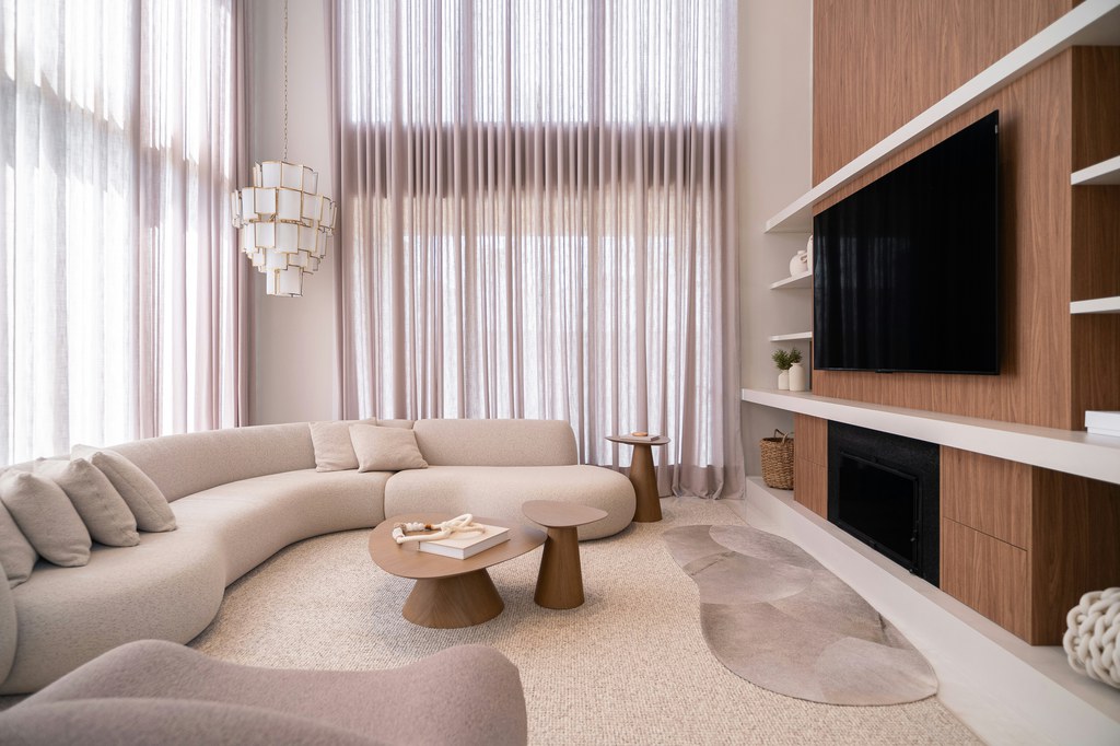 Curved beige sectional sofa with round wood coffee tables in a modern living room with a wall-mounted TV.