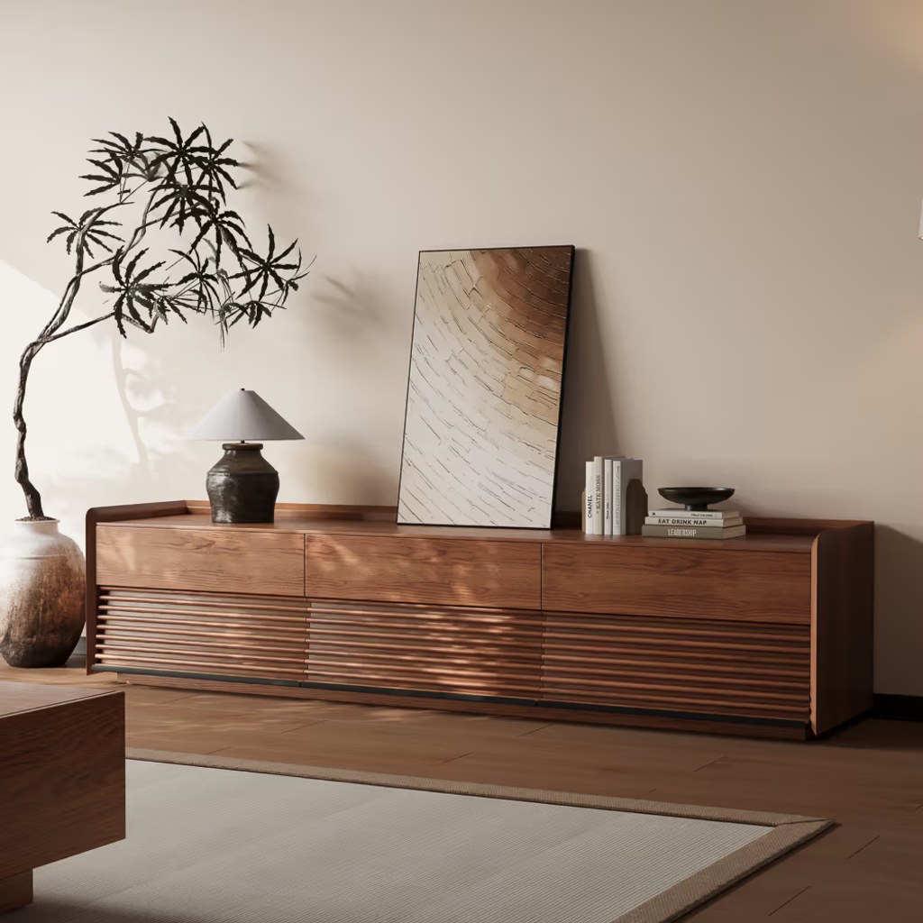 Low-profile walnut media console with slatted cabinet doors, drawers, books, a table lamp, and framed artwork.