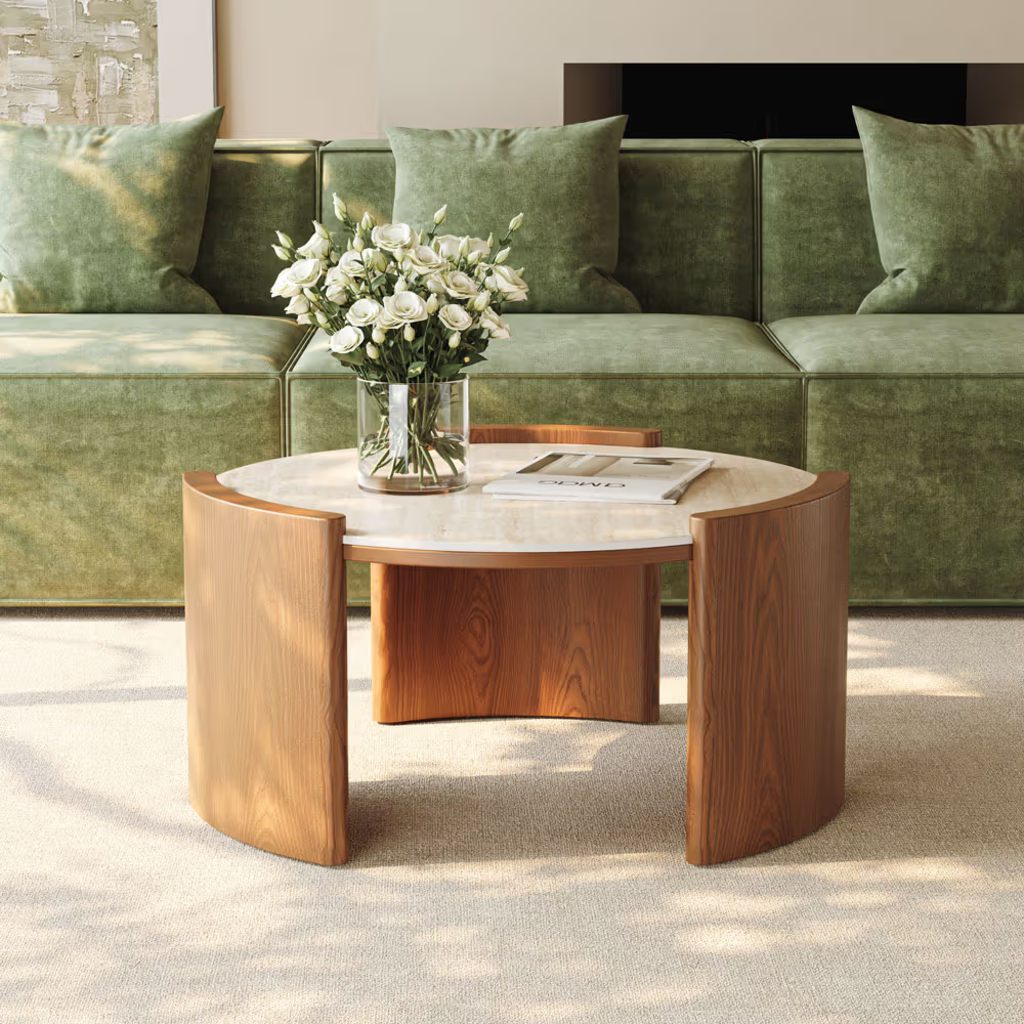 Round walnut coffee table with a light stone top in front of a green sofa.