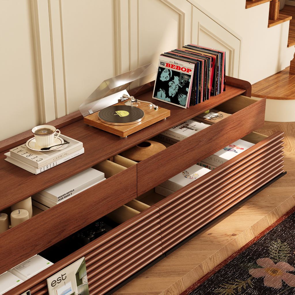 Low-profile walnut TV stand with open storage drawers, a record player, vinyl records, books, and media accessories.