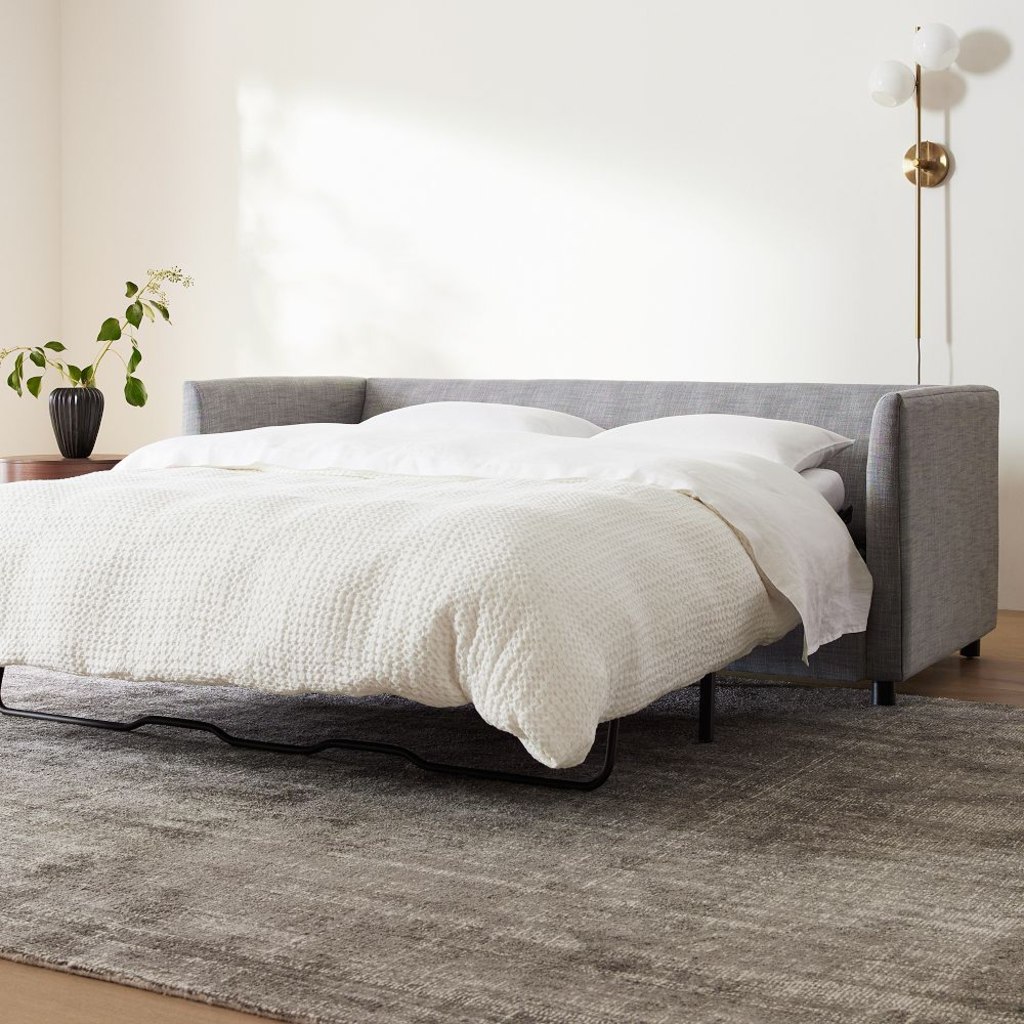 Gray sleeper sofa opened into a bed with white bedding in a bright, modern living room.