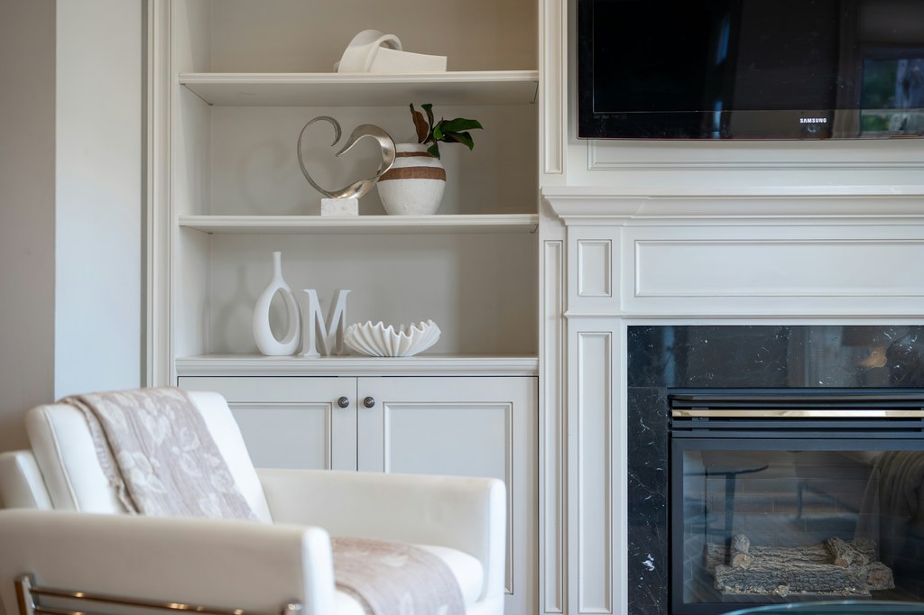 White recliner beside a fireplace and built-in shelving in a bright living room.