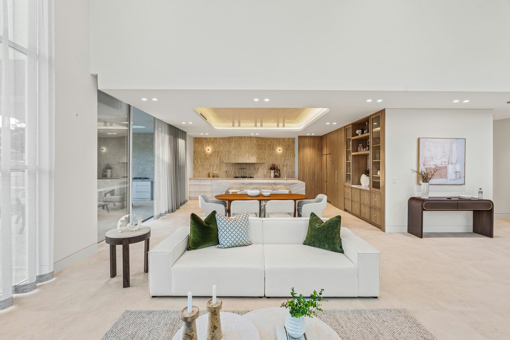 Modern open-plan living room with white sofa, green accent pillows, wooden dining area, built-in storage, and minimalist interior design.
