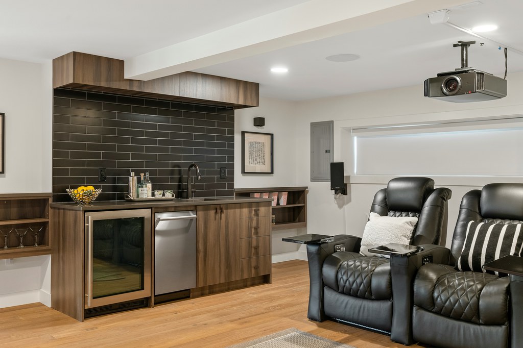 Black leather recliner chairs in a home theater room with a ceiling-mounted projector and wet bar.