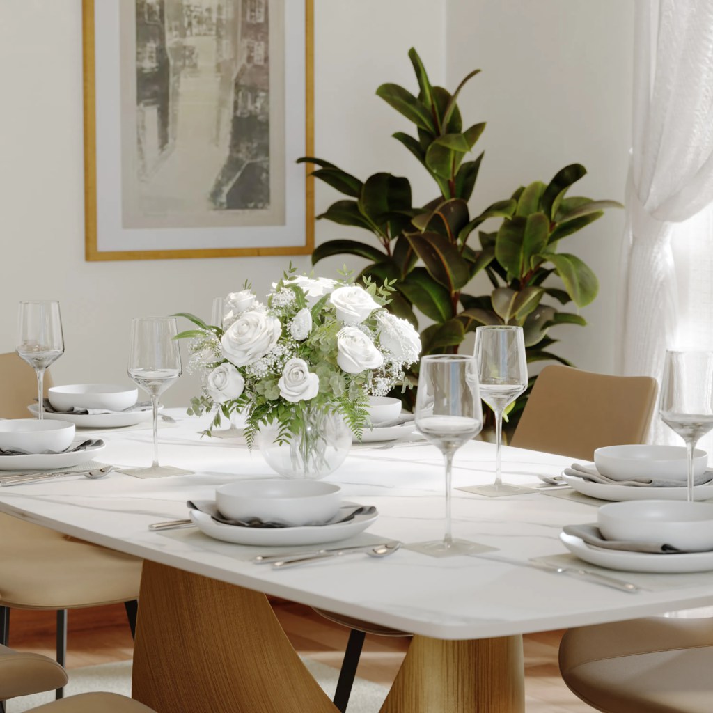 White dining table set for six with beige chairs, glassware, and a floral centerpiece in a bright modern dining room.