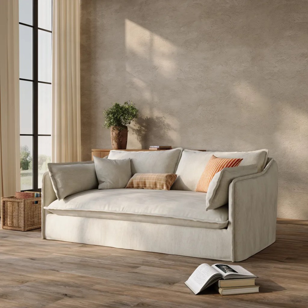 Cream bench-seat sofa with one continuous cushion and loose pillows in a sunlit neutral living room.