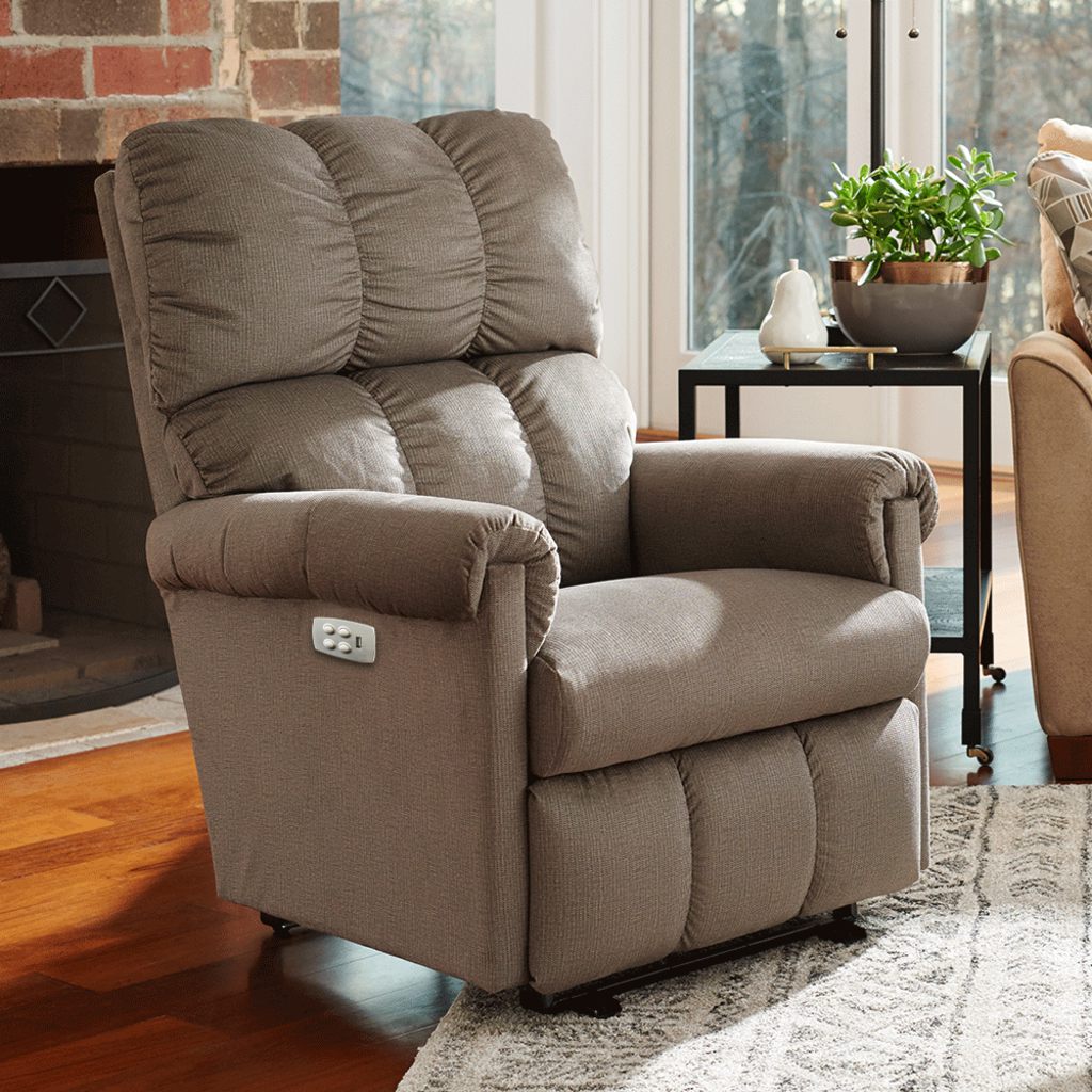 Gray upholstered power recliner chair with padded back and armrests in a bright living room.