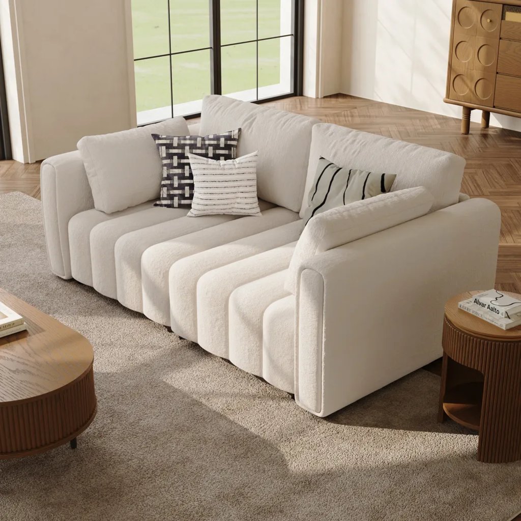 Cream tufted bench-seat sofa with decorative pillows in a bright modern living room.
