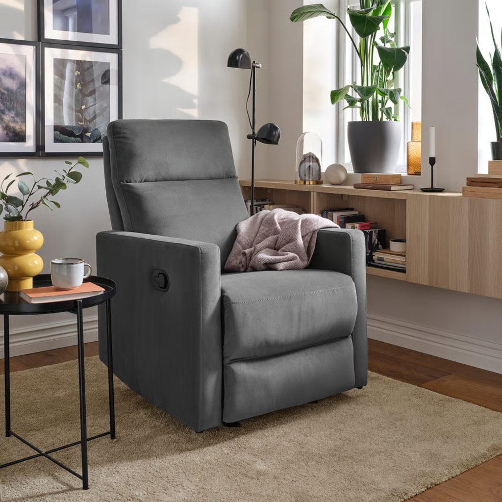 Gray manual recliner chair with a side lever in a bright living room with plants and a side table.