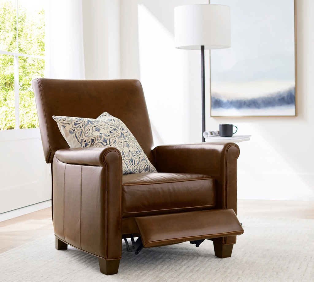 Brown leather recliner chair with extended footrest and patterned pillow in a bright living room.