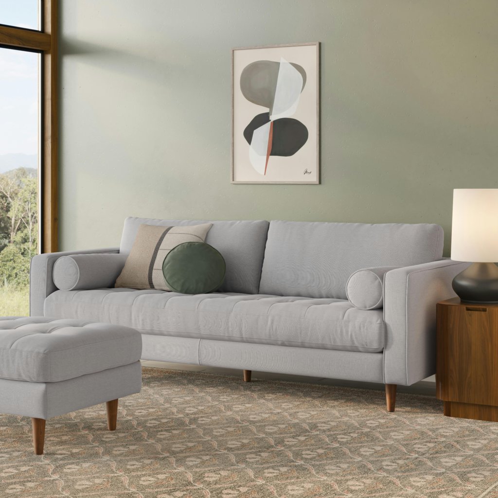Light gray tufted bench-seat sofa with bolster pillows and a matching ottoman in a modern living room.